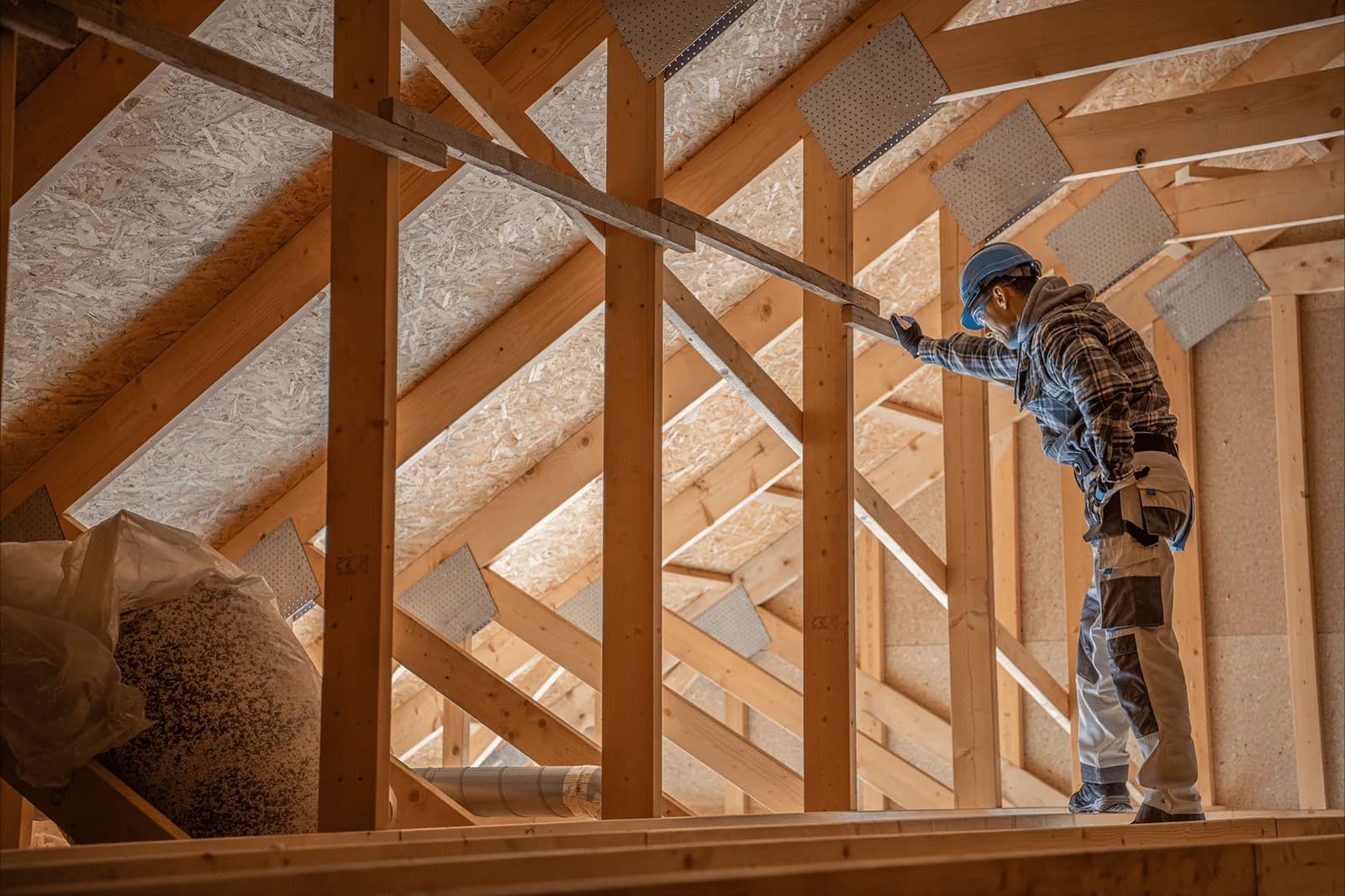 Worker using a hose to install insulation between exposed timber roof members