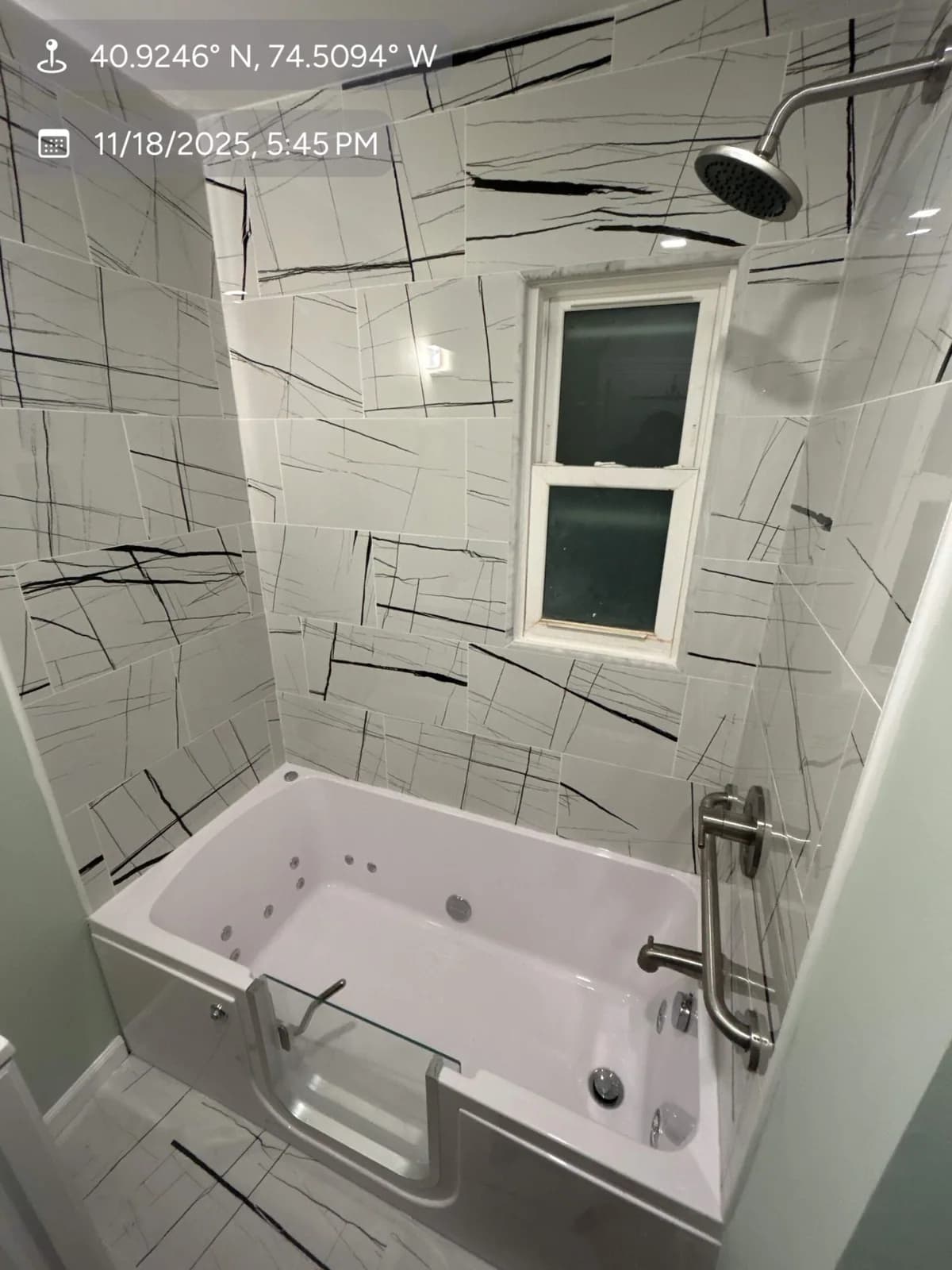 Bathtub and shower surround finished in large white patterned tiles beneath a window