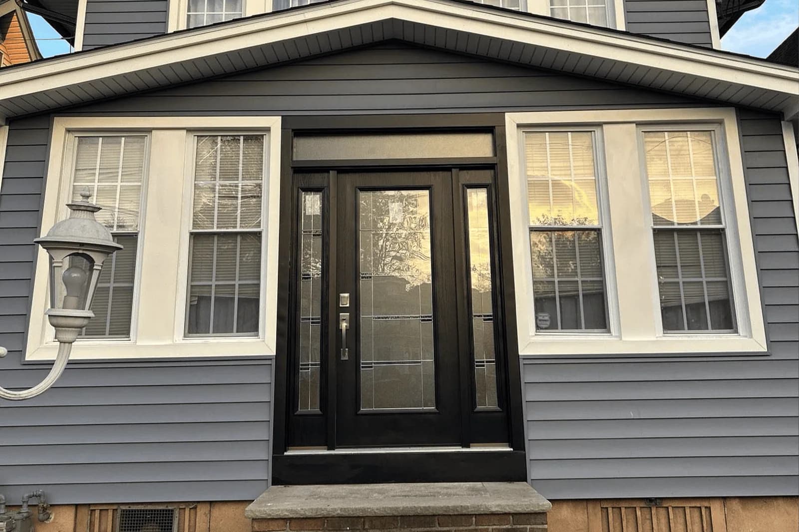 Dark glazed entry door flanked by white-trimmed windows and gray siding