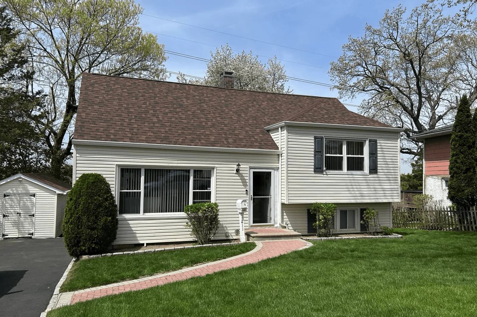 Light-colored split-level home with a brown shingle roof and white gutters along the eaves