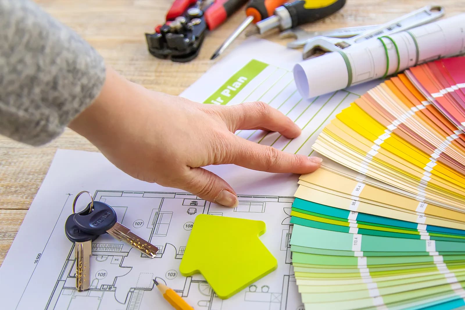 A hand comparing a fan of paint colors over renovation plans