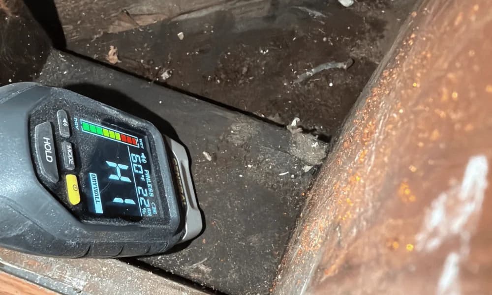 Handheld moisture meter positioned against an exposed building material