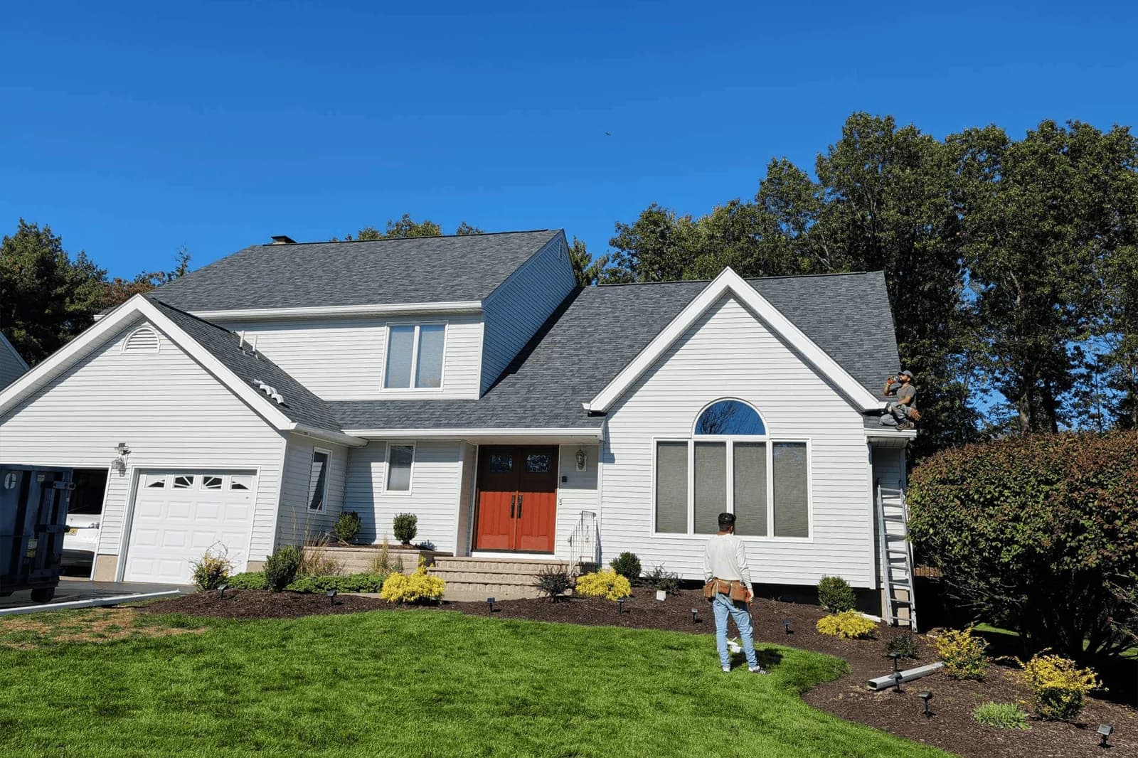 Light-colored house with an asphalt shingle roof and contrasting orange entry door