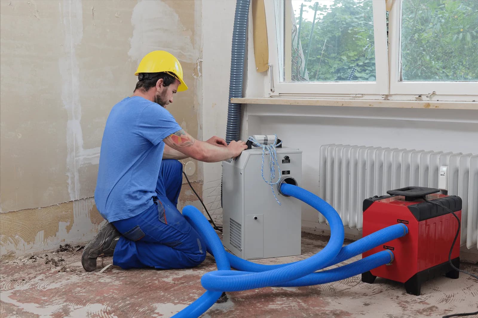 Technician working with restoration equipment beside a stripped interior wall