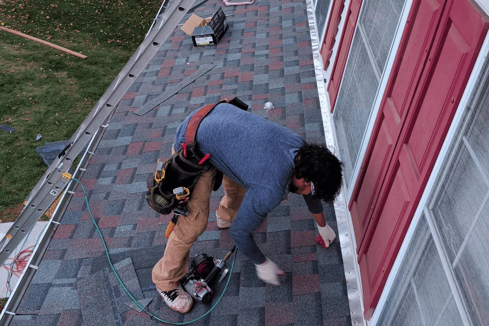 Roofer working on shingles beside an upper-story wall and window