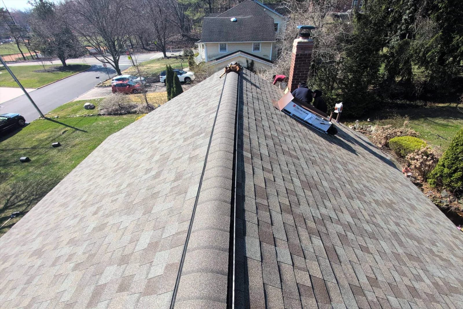 View along a shingle roof ridge toward a brick chimney and its flashing