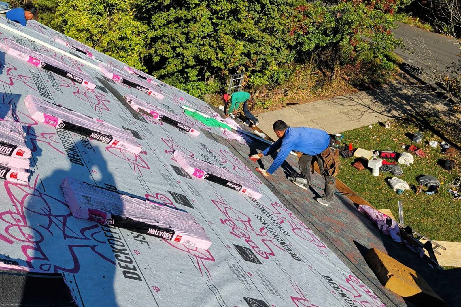 Roofing crew laying shingles beside exposed underlayment on a pitched roof