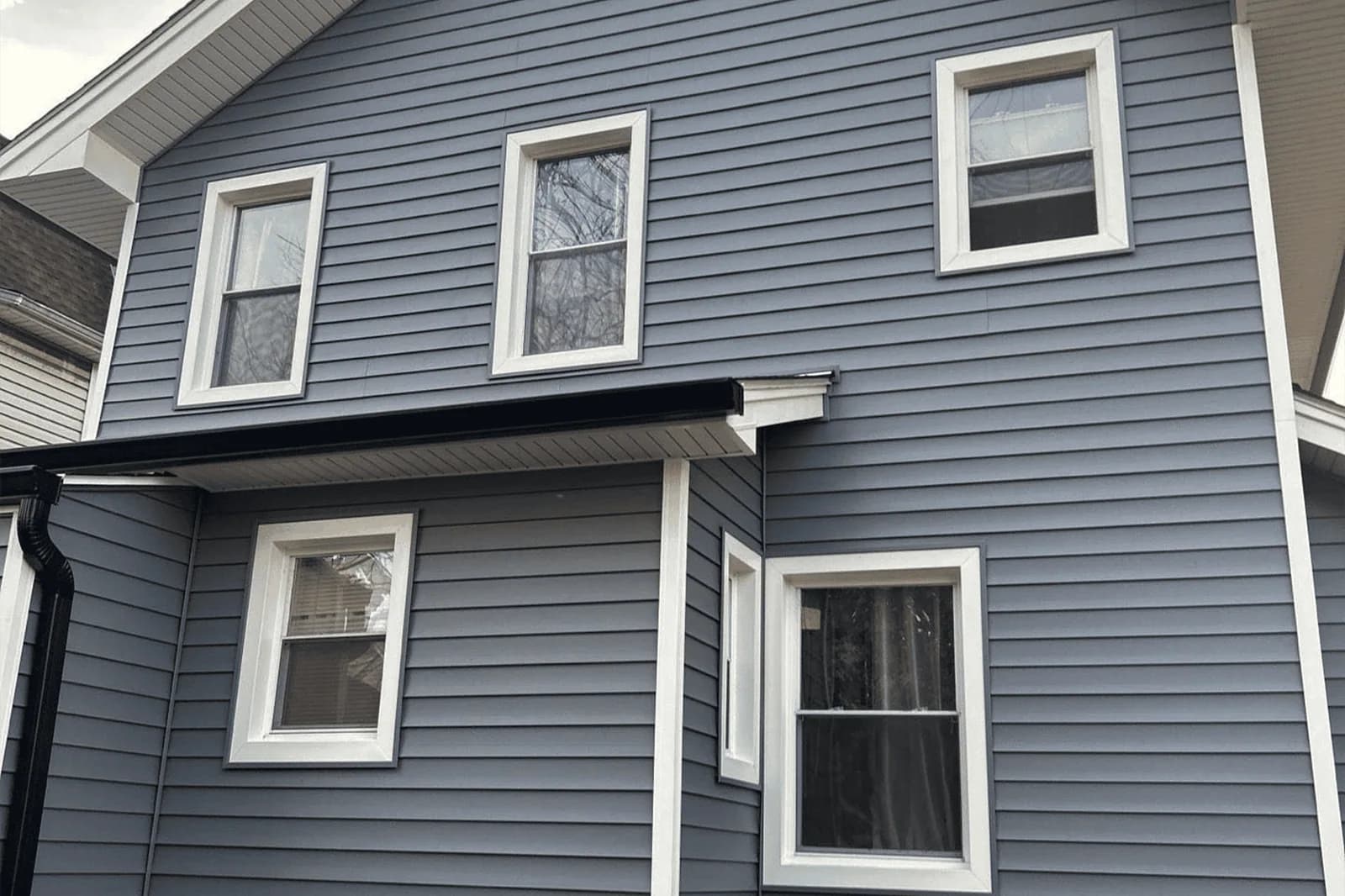 Gray-sided house with white window trim, a small entry roof, gutter, and downspout