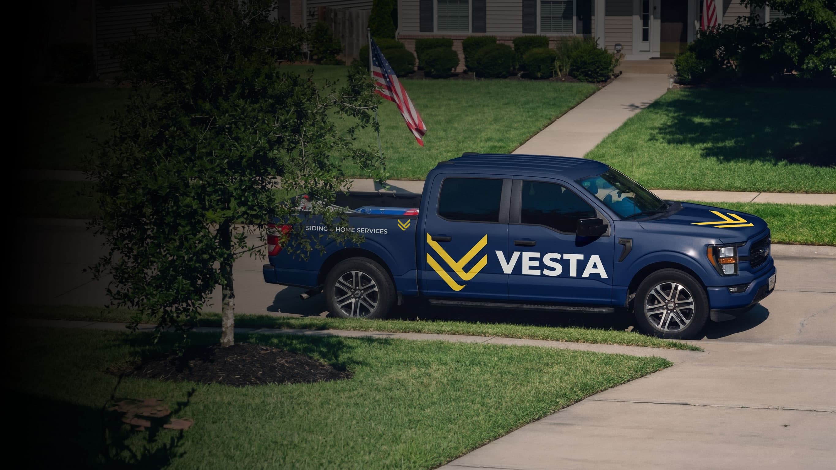 Navy Vesta pickup truck with the yellow chevron and white Vesta lettering, parked outside a home